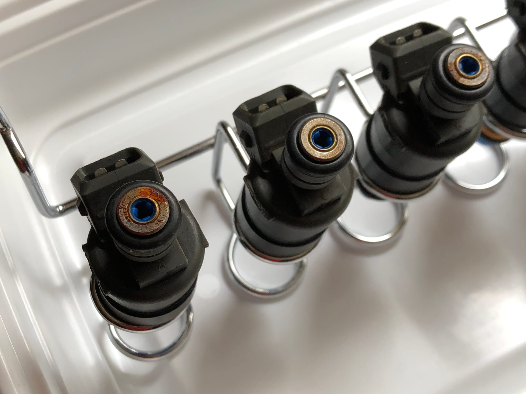 Four Porsche 944 fuel injectors lined up in a tray